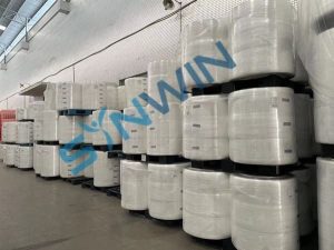 Lager fyllt med stora rullar av vitt tygmaterial, redo för produktion av tygpåsar.